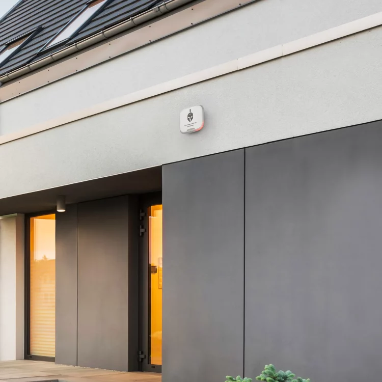 Façade de maison avec porte d’entrée sombre et alarme de sécurité connectée installée sur le mur extérieur.
