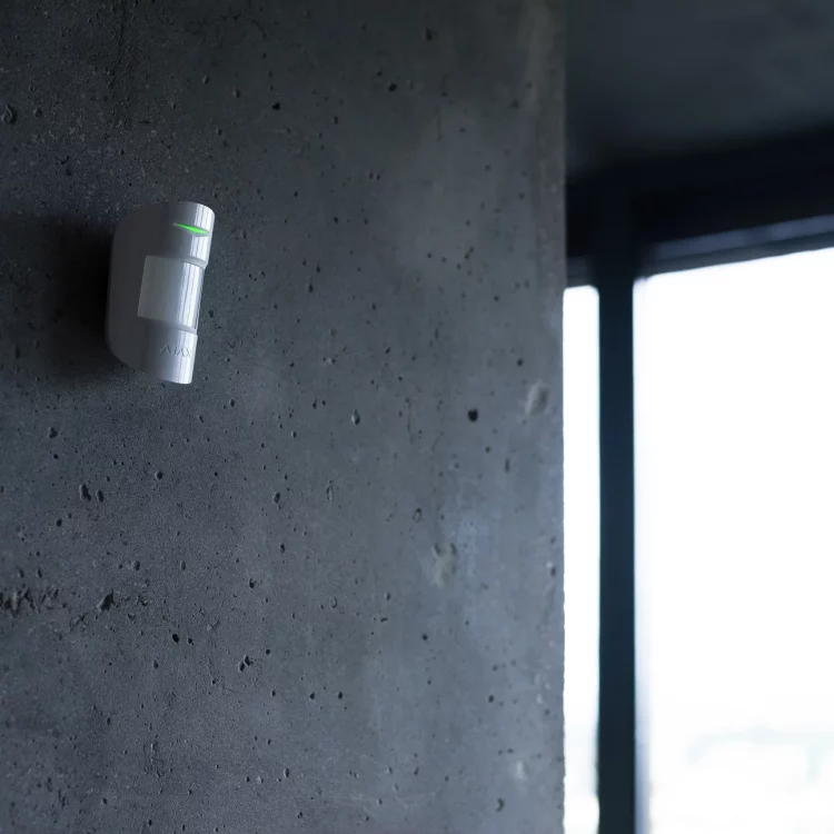 Détecteur de mouvement fixé sur un mur en béton, avec voyant lumineux actif en intérieur.